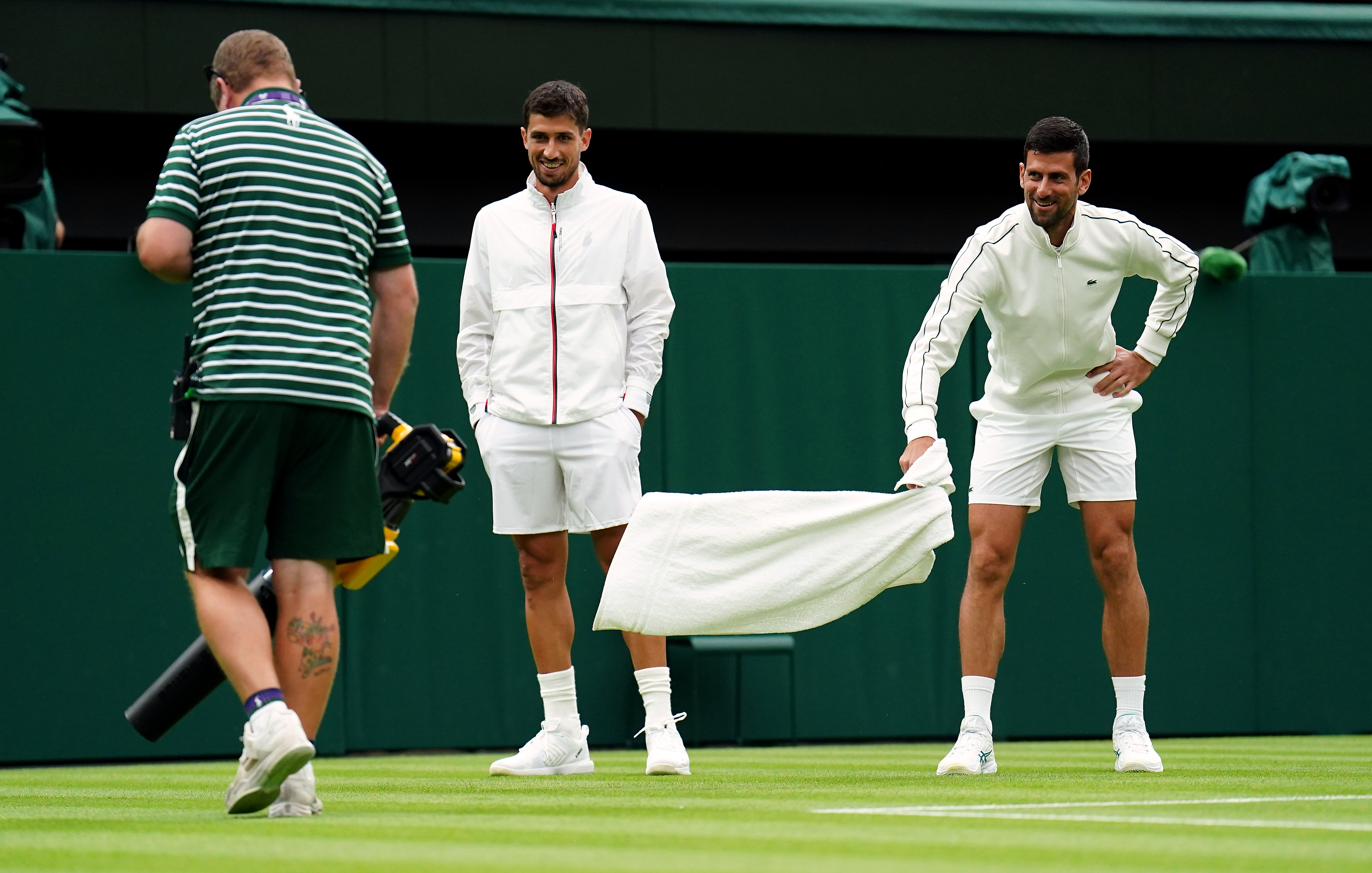 Novak Djokovic watches the ground staff try and dry the court