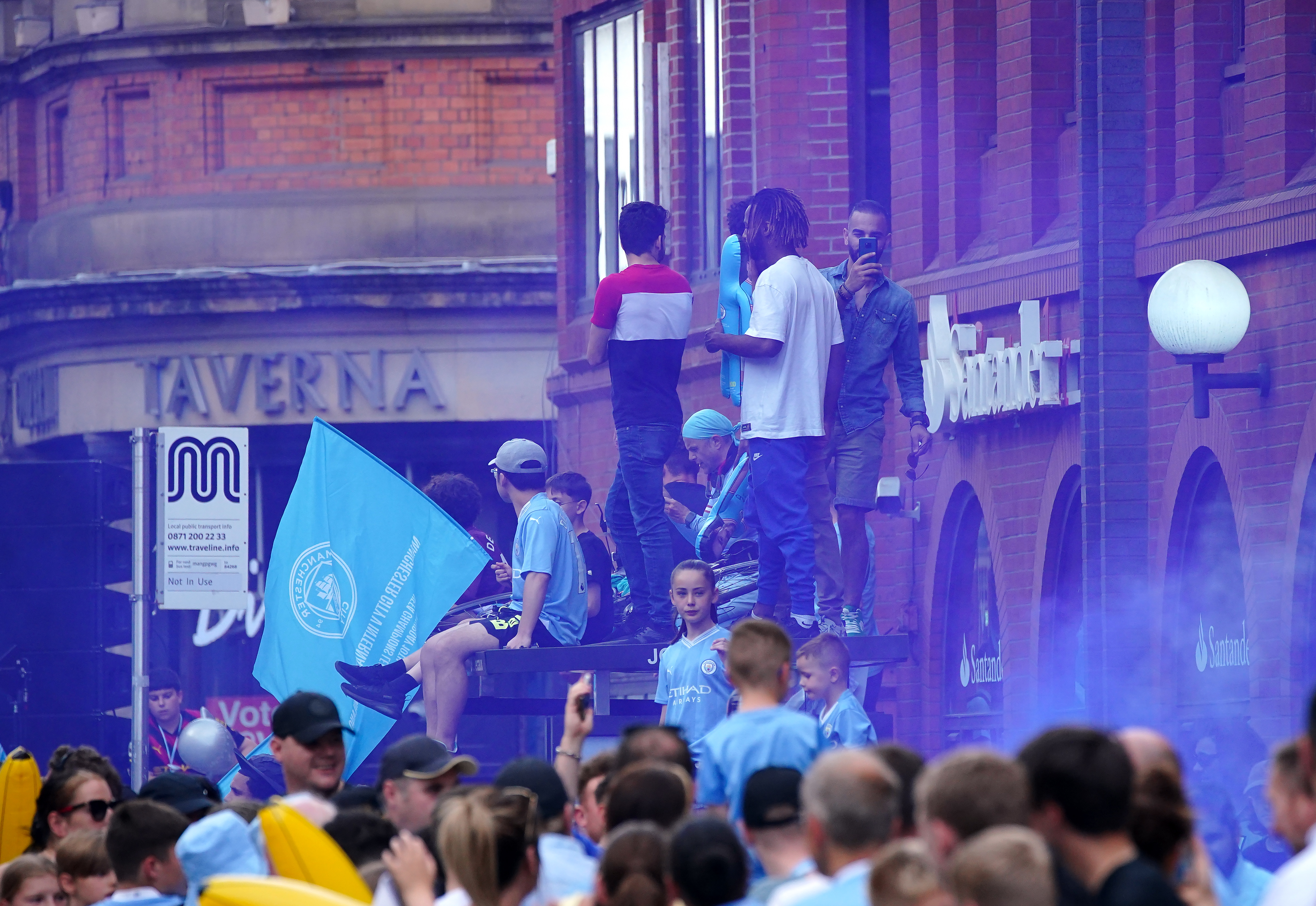Manchester City fans stand on a bus stop ahead of the treble parade
