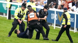 A protester is escorted off the track by police and stewards at Epsom (Mike Egerton/PA)