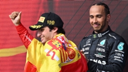Carlos Sainz, draped in a Spanish flag, celebrates as Lewis Hamilton looks on