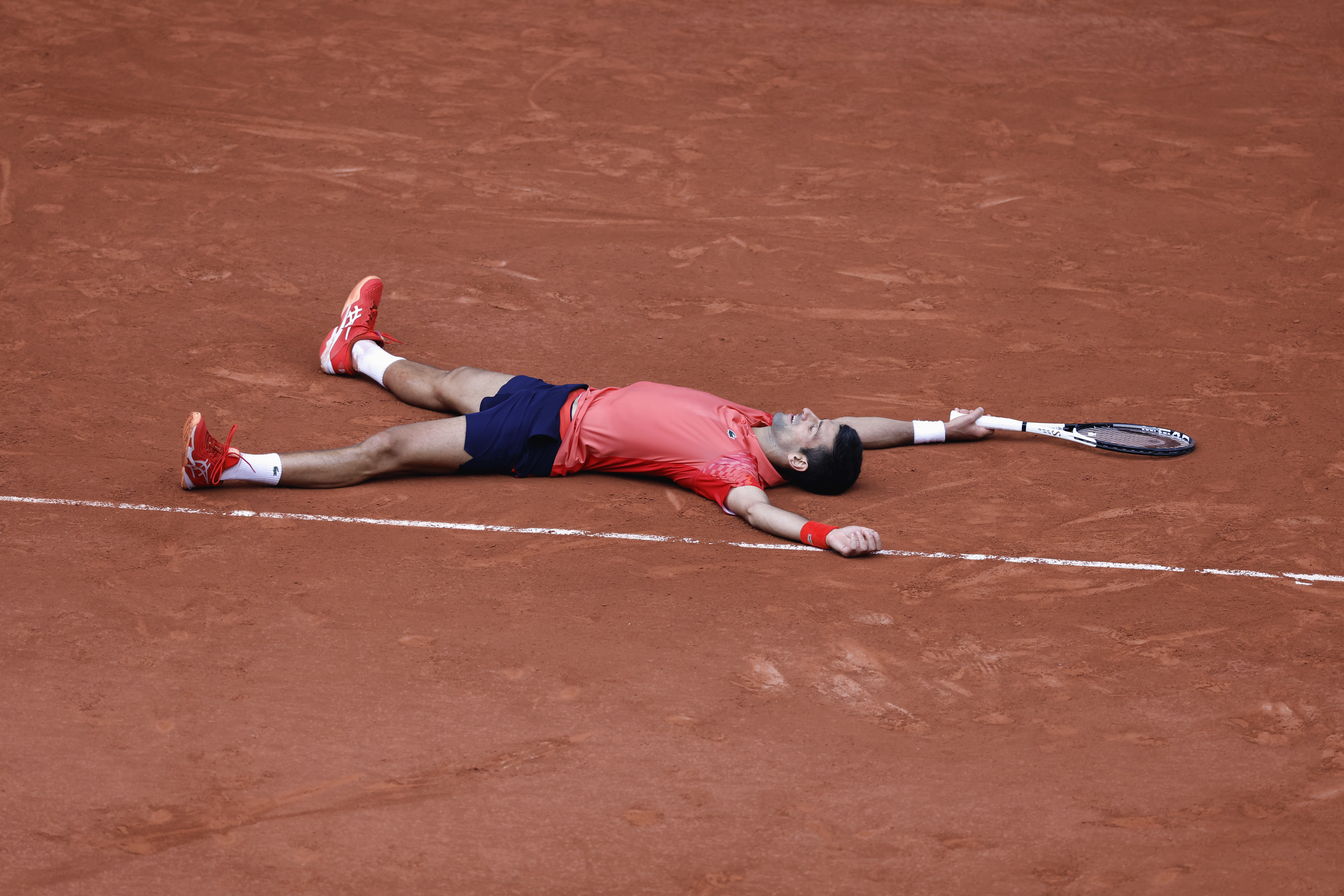 Novak Djokovic lies on the clay after Casper Ruud's final shot flies wide